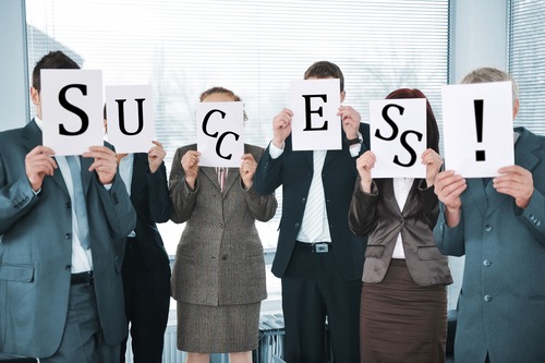 Businesspeople holding white papers in the office that spell Success